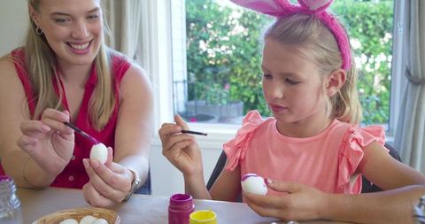 Woman and girl painting easter eggs together at home, family craft activity, spring bonding