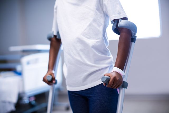 Mid section of girl walking with crutches in ward of hospital