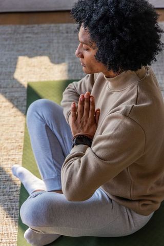 African american man meditating on yoga mat in sunlight at home for wellness