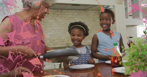 Grandmother serving pancakes to smiling children at kitchen counter with syrup