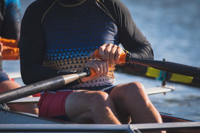 Senior man engaging in rowing activity on a river, holding oars with both hands. Ideal for illustrating active retirement lifestyles, senior fitness, water sports, and teamwork in outdoor settings.
