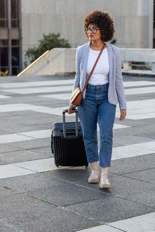 African american woman walking across urban plaza pulling suitcase and glancing left