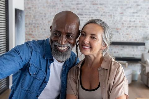Mature couple smiling taking selfie on sofa in modern bright loft living room
