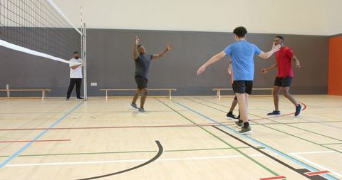 Multiethnic male teammates playing indoor volleyball and celebrating point on gym court