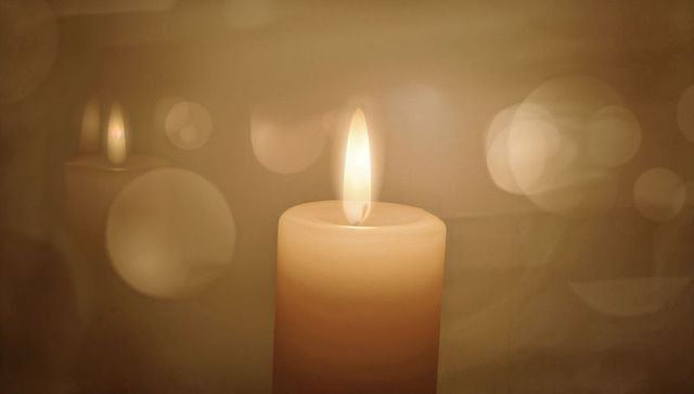 Glowing cream pillar candle emitting gentle flame with bokeh orbs and warm sepia mood