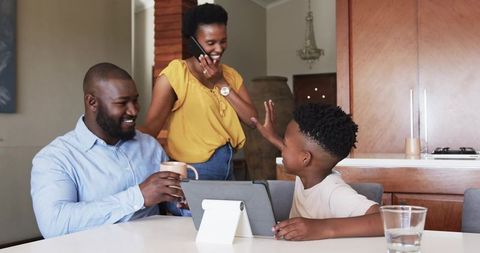 African American family sharing morning coffee, smiling and waving with tablet in kitchen