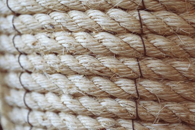 Close-up view of tightly coiled hemp rope showcasing its rough texture and natural fibers. This image is useful for projects focusing on adventure, nautical themes, or robustness. It can serve as a background for websites, marketing materials, or blogs discussing natural materials, traditional craftsmanship, or outdoor activities.