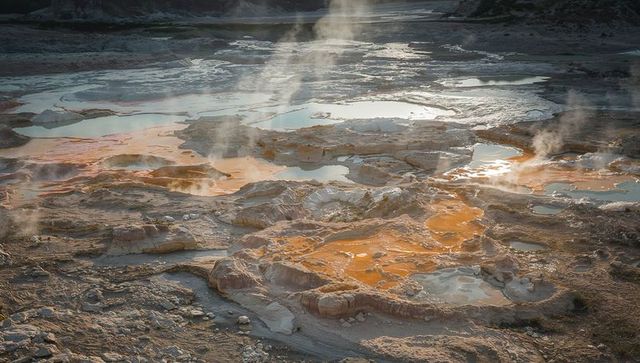 Aerial view of steam rising from colorful geothermal terraces