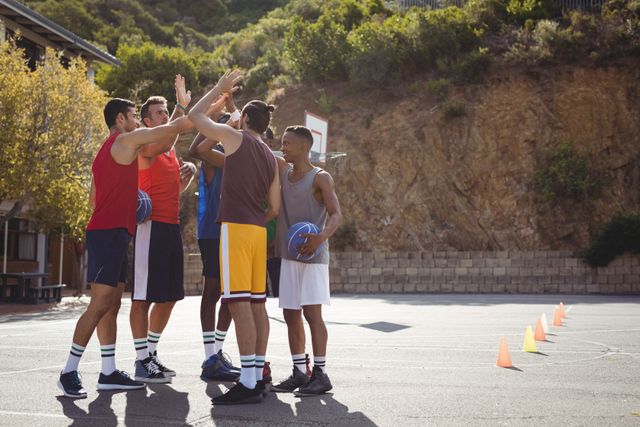 Group of basketball players giving high-fives on an outdoor court, showcasing teamwork and celebration. Ideal for use in sports-related content, promoting teamwork, fitness, and active lifestyles. Suitable for advertisements, social media posts, and articles about youth sports and outdoor activities.