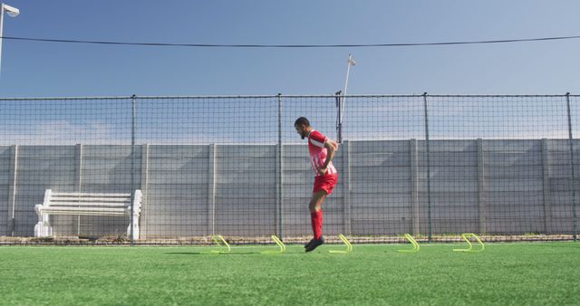 Biracial male football player wearing red uniform training on outdoor pitch. Football, sports and fitness.
