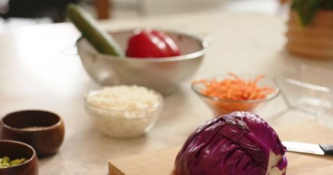 Halved Purple Cabbage Sitting on Wooden Cutting Board with Bowls of Shredded Carrot and Rice