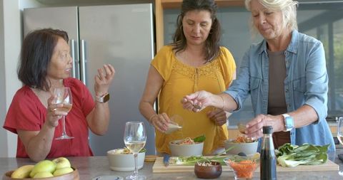 Mature women preparing healthy meal together in bright kitchen sharing conversation and wine