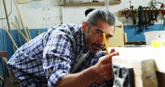 An experienced male artisan is marking a wooden plank with intense focus in a workshop. This image can be used in articles or advertisements related to carpentry, woodworking, craftsmanship, or manual labor. It demonstrates precision and dedication in skilled work.