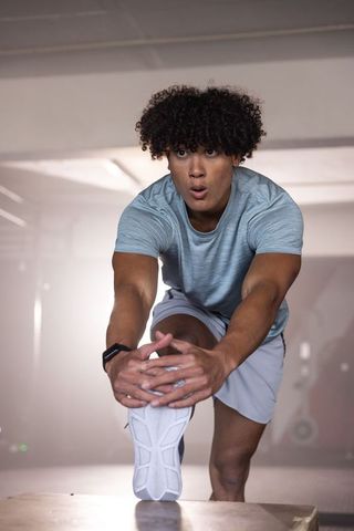 African american man stretching on plyometric box in gym wearing gray athletic wear