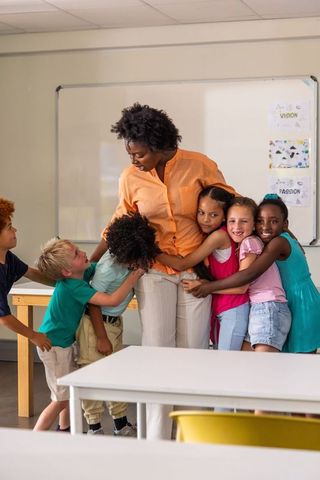 African american teacher hugging smiling diverse elementary students in classroom