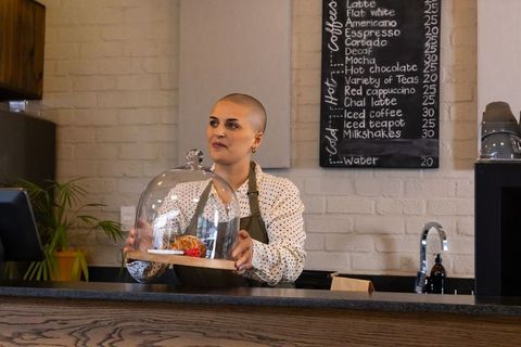 Barista presenting pastry under glass cloche on wooden counter in cozy urban cafe