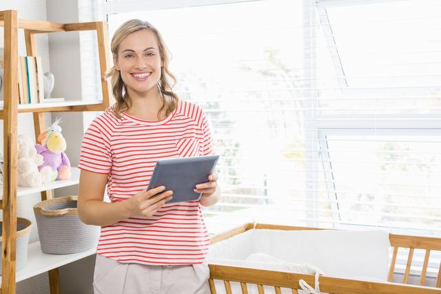 Smiling woman holding a digital tablet in a bright, modern home. Ideal for use in lifestyle, technology, and home office productivity contexts. Perfect for illustrating modern living, casual work environments, and the integration of technology in daily life.