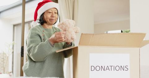 Senior woman donating teddy bear at home during festive season