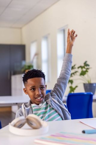African american boy raising hand in classroom showing engagement and confidence