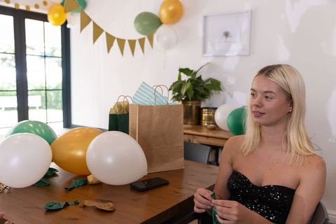 Young woman preparing birthday decorations at home with gold and green balloons and gifts
