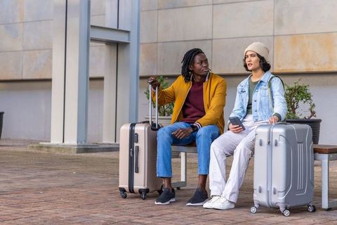Diverse travelers waiting on urban bench with suitcases checking smartphone planning trip