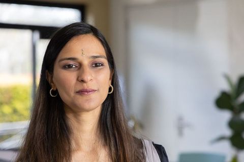 Indian woman standing and looking left wearing bindi and gold hoop earrings in living room