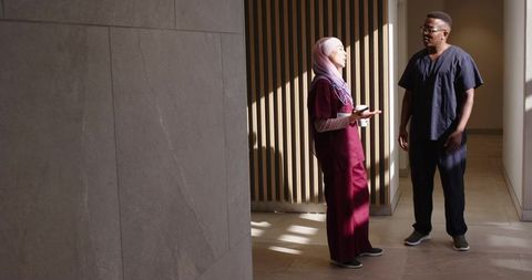 Diverse clinicians discussing patient chart in sunlit hospital corridor, teamwork and care