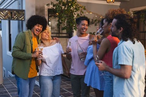 Friends laughing and toasting with champagne on outdoor terrace under string lights