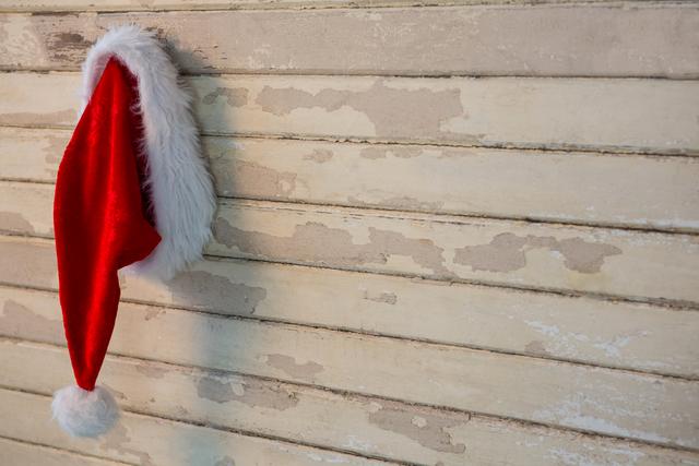 Santa hat hanging on a rustic wooden wall, evoking a festive and cozy holiday atmosphere. Ideal for use in Christmas-themed advertisements, holiday greeting cards, festive blog posts, and seasonal social media content.