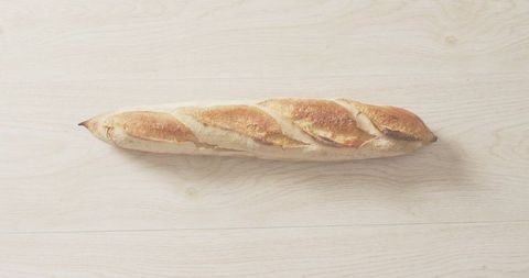 Rustic baguette resting on pale wooden tabletop showing golden crust and scoring
