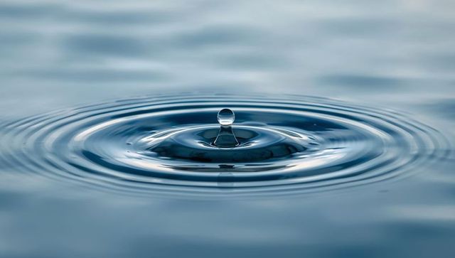 Glassy Water Droplet Creating Concentric Ripples on Calm Blue Surface Macro Minimalist