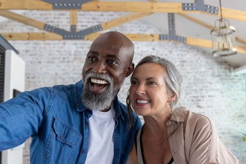 Mature couple taking selfie in bright renovated loft with exposed brick and wooden beams