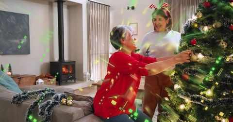 Senior woman decorating christmas tree with adult daughter holding gold bauble in cozy living room
