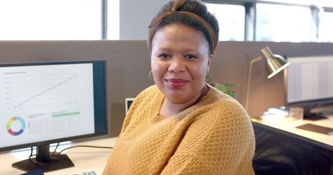 Mid-adult African American woman smiling at desk viewing analytics on monitor in office