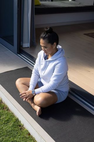 Woman practicing mindful meditation on exercise mat spanning sliding door threshold