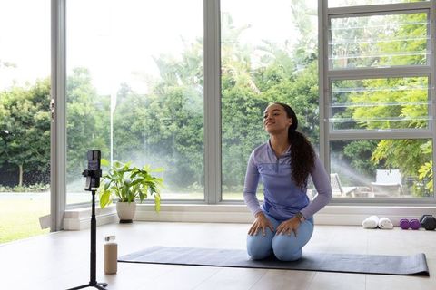 African american woman recording yoga class on smartphone tripod in sunlit home studio