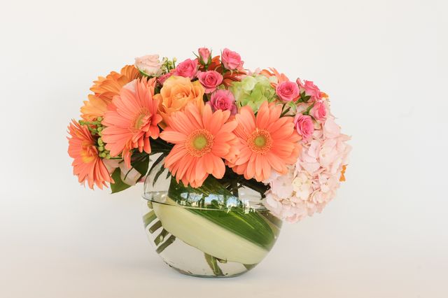 This image of a vibrant floral arrangement featuring orange daisies, pink roses, and green foliage in a clear glass vase is ideal for use in home decor magazines, DIY decoration blogs, and floral shop advertisements. The elegant and colorful bouquet can also be used in wedding planning websites and event decorating guides to inspire stylish centerpiece ideas.