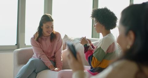 Multicultural Friends Sharing Sunlit Sofa Moments While Checking Smartphone Casual Home Gathering