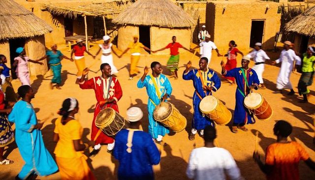 Village drummers leading circle dance in sunlit courtyard, colorful traditional robes