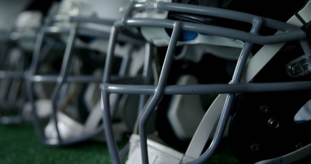 This image showcases a close-up view of several football helmets lined up on field turf, offering a detailed look at the sports equipment used in American football. Ideal for websites and promotions related to sports gear, youth sports leagues, athletic safety, and football training programs.