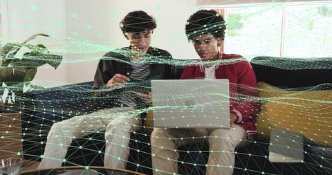 Two young men collaborating on laptop and tablet with augmented reality digital mesh overlay