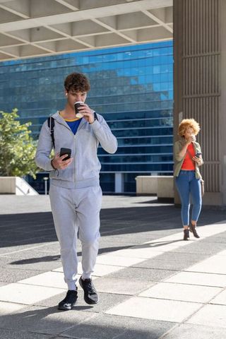 Young man and woman walking through urban plaza sipping coffee and using smartphones
