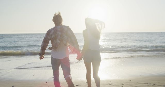 Happy caucasian couple holding hands on beach at sunset. Vacations, romance, love nature and relaxation, unalterned.