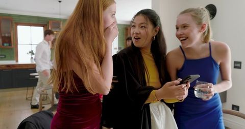 Diverse friends reacting to smartphone surprise laughing and gasping at home party