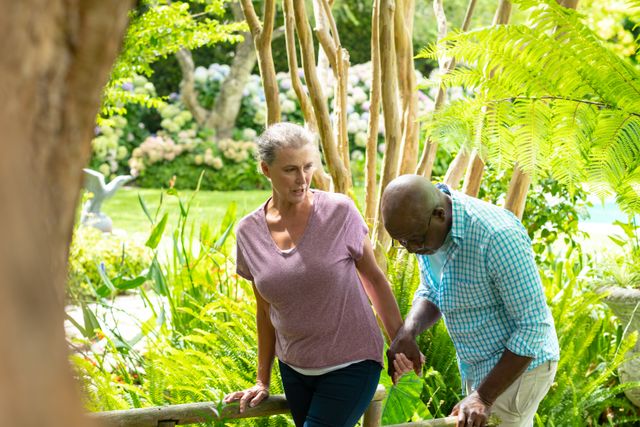 Senior couple enjoying a walk in a lush backyard garden, holding hands and surrounded by greenery. Ideal for use in lifestyle, retirement, and nature-themed projects, as well as promoting healthy and active aging.
