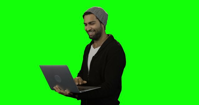 Man smiling and using laptop with green screen background, perfect for tech advertisements, website banners, or promoting digital products. Ideal for illustrating remote work, online communication, or tech-related projects.