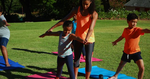 Diverse group of adults and children practicing yoga outside on colorful mats in park. Active lifestyle and fitness. Suitable for content about family activities, healthy living, outdoor exercises, and youth fitness programs.