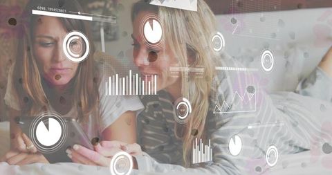 Two women relaxing bed utilizing smartphone with modern data interface