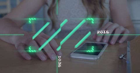 Woman interacting with smartphone displaying futuristic green HUD overlay on wooden desk