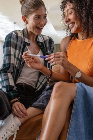 Joyful female couple celebrating positive pregnancy test result